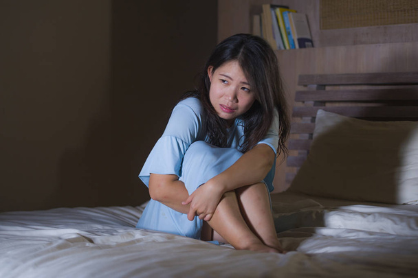 dramatic portrait of young beautiful and sad Asian Chinese woman crying desperate on bed awake at night suffering depression crisis and insomnia feeling pain and broken heart - Photo, Image