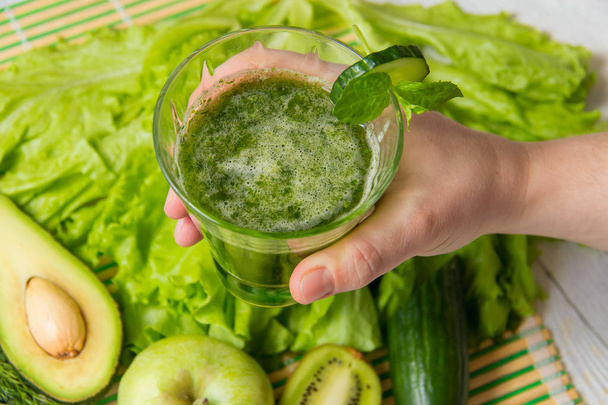 Hand hold healthy green smoothie against ingredients on wooden background - Foto, immagini