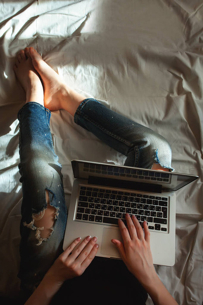 Draufsicht der Bloggerin, die zu Hause auf dem Bett sitzt, mit faltiger weißer Wäsche auf der Laptop-Computertastatur tippt, einen Artikel schreibt, leeres Bildschirm-Smartphone, Kaffee trinkt. - Foto, Bild