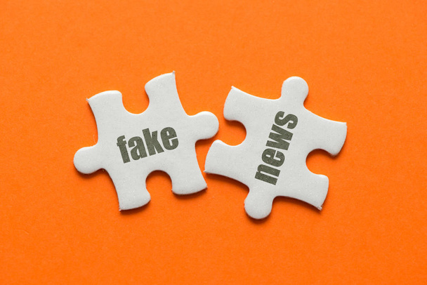 zwei weiße Puzzledetails mit Text Fake News auf orangefarbenem Hintergrund, Nahaufnahme. - Foto, Bild