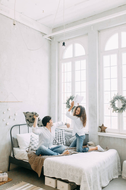 Young couple hugging and fighting not the bed. Photo shoot in bright interior Studio in European style. - Φωτογραφία, εικόνα