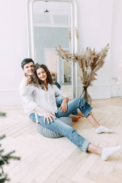 Young couple embracing and sitting in front of a mirror. Photo shoot in bright interior Studio in European style. - Фото, изображение