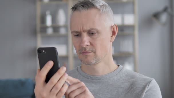 Triste hombre de pelo gris reaccionando a la pérdida en línea en el teléfono inteligente
 - Metraje, vídeo