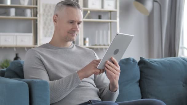 Gri saçlı adam Internet Tablet kanepede otururken tarama - Video, Çekim