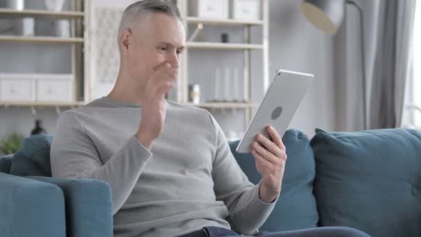 Online Video Chat na tabletu šedivé vlasy muž relaxační na gauči - Záběry, video