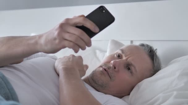 Grijs haar Man reageren op verlies tijdens het gebruik van Smartphone in Bed - Video