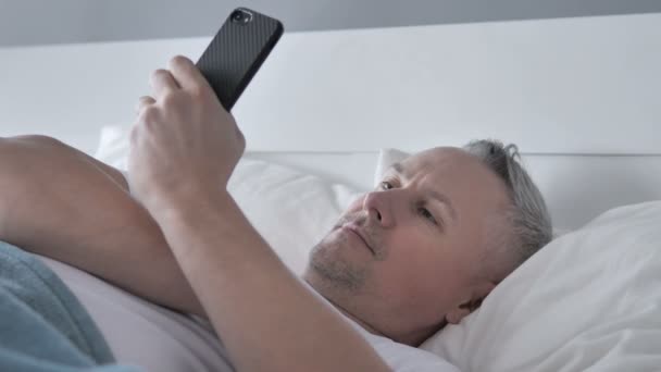 Gri saç adam kullanma Smartphone Lying yatakta iken - Video, Çekim