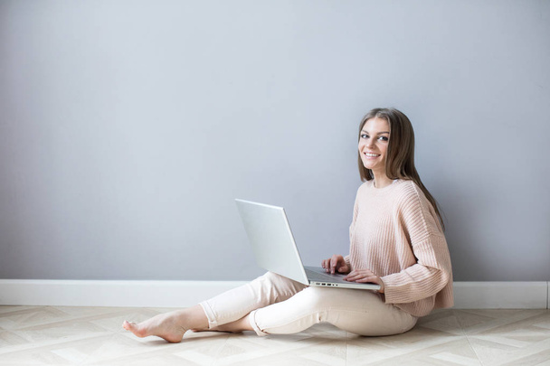 Lächelnde junge Frau mit Laptop, die auf einem Holzboden sitzt. Freiberufler. - Foto, Bild