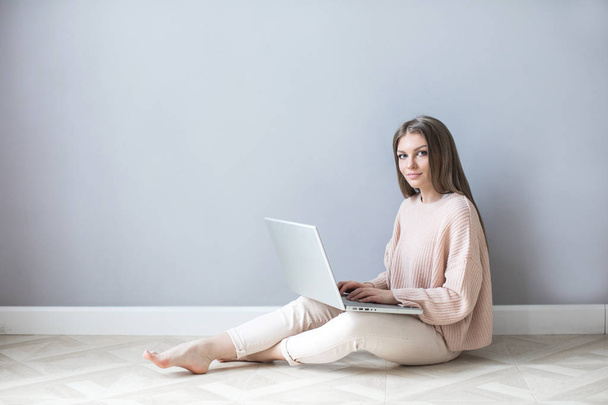 Young woman using a laptop sitting on a wooden floor. Freelancer. - Φωτογραφία, εικόνα