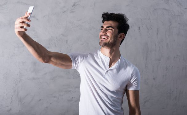 A happy young man taking a selfie with his smartphone in a white - Foto, imagen