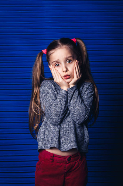 sad little girl holding her cheek on a blue background. child toothache concept. - Photo, Image