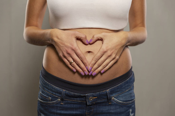 Embarazo temprano, manos en forma de corazón en el estómago, primer plano
 - Foto, imagen