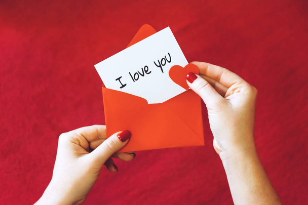 Valentines day card ideas. Greeting card with red envelope in womens hands. Female hand with white card and text I love you on red background. Love, romance concept - Fotografie, Obrázek
