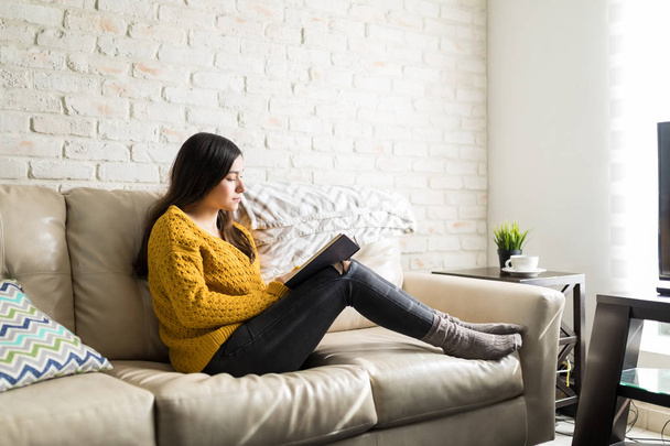 家で座りながら小説を読むことに興味を示す女性の完全な長さ - 写真・画像