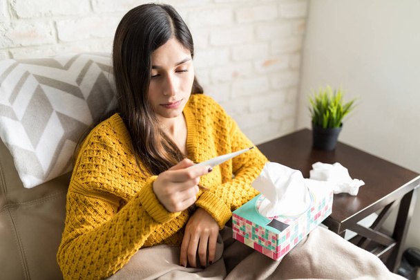 Unwell woman looking at thermometer while suffering from high fever during winter - Foto, Imagem