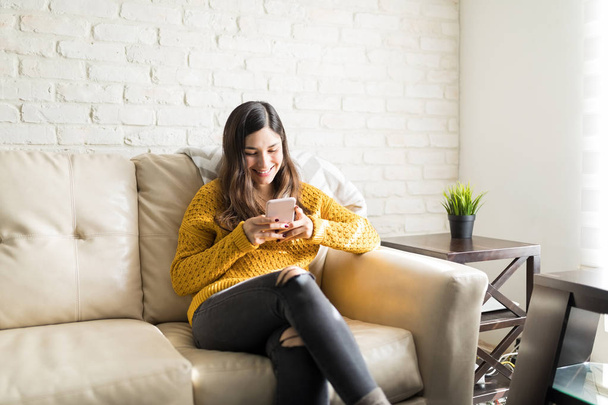 Расслабленная молодая женщина с помощью приложения обмена сообщениями на смартфоне дома
 - Фото, изображение