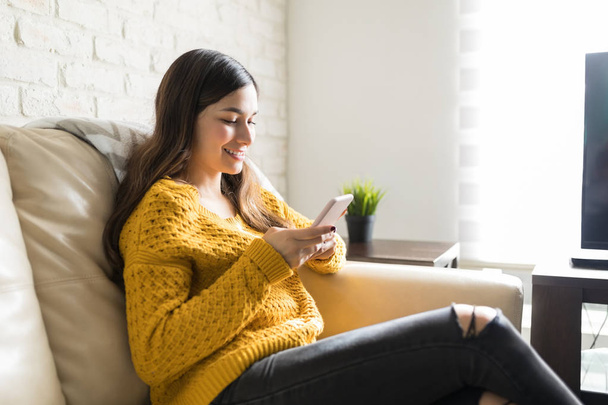Mujer bonita sonriendo mientras usa el teléfono móvil para conectarse con amigos en casa
 - Foto, Imagen