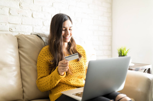 Carefree woman purchasing online using wireless computer on sofa at home - Foto, imagen