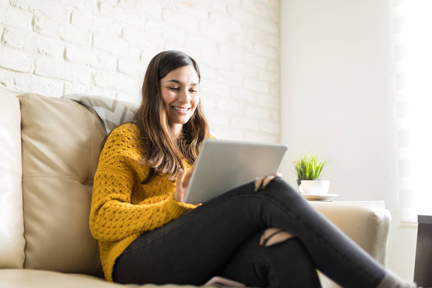 Uśmiechający się łaciński brunetka za pomocą serwisów społecznościowych na cyfrowy tablet w domu - Zdjęcie, obraz