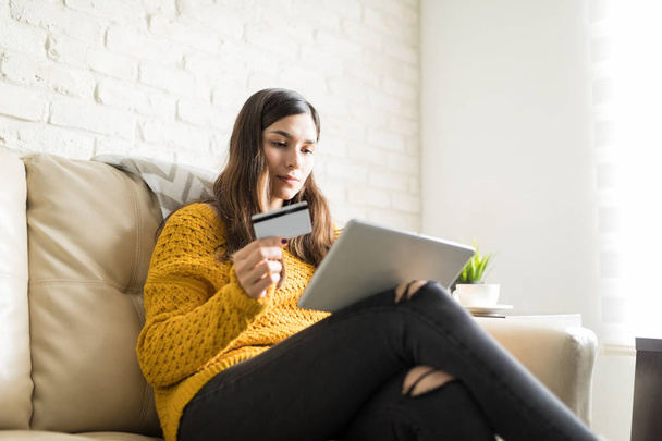 Charming woman using credit card and portable PC on sofa in living room - Foto, afbeelding