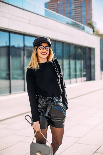 young attractive stylish smiling woman having fun in city , positive, emotional, long hair, wearing leather shorts and black sweatshirt bright red lips. - Fotografie, Obrázek