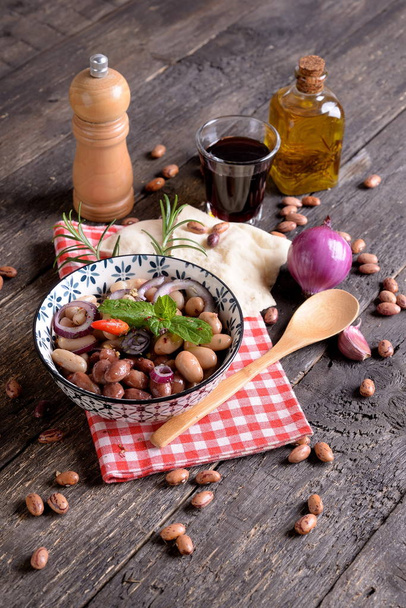 Чаша с римской фасолью с луком, травами и оливковым маслом на столе
 - Фото, изображение