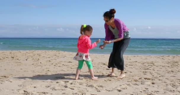 famiglia di donna madre o babysitter e bambino o ragazza di quattro anni, che cammina e cerca, raccogliendo e raccogliendo conchiglie sulla spiaggia di sabbia, a Bolonia Beach, Cadice, Andalusia, Spagna, Europa
. - Filmati, video