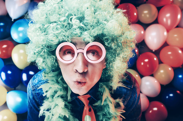 Young man in blue wig and glasses posing against colorful party balloon background - Photo, image