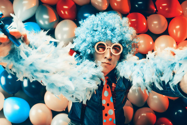 Young man in blue wig and glasses posing against colorful party balloon background - Φωτογραφία, εικόνα