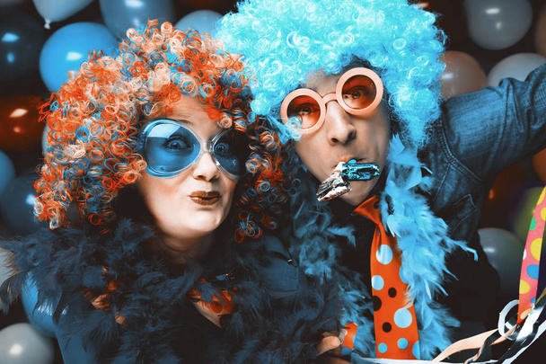 Funny young couple in colorful wigs and glasses having fun against colorful party balloon background - Фото, изображение