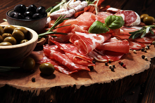 Planche à découper en marbre avec prosciutto, bacon, salami et saucisses sur fond bois. Amuse-gueule et olives
 - Photo, image