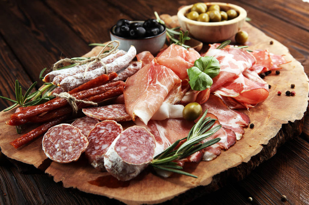 Marmeren snijplank met ham, spek, salami en worstjes op houten achtergrond. Vlees schotel hapjes en olijven - Foto, afbeelding