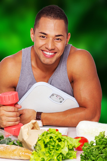 homem saudável bonito com alimentos, escalas e halteres
 - Foto, Imagem