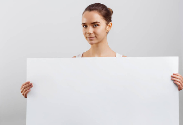 Portrait of a beautiful brunette woman holding a white blank banner. - Foto, afbeelding