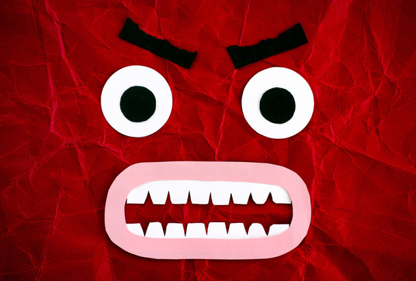 Angry emotional face made from paper. Red background. Close-up. - Foto, Imagem