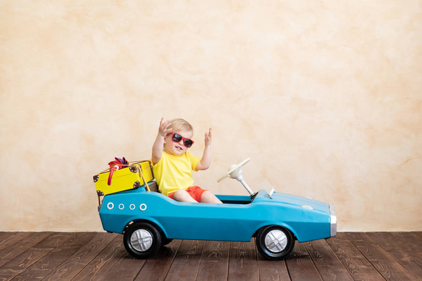 Happy child riding toy vintage car. Funny kid playing at home. Summer vacation and travel concept - Foto, Imagen