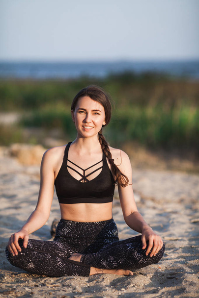Happy smile Slim young Woman In Lotus Position looking at camera At sand beach. Copy space. Healthy style sport - 写真・画像