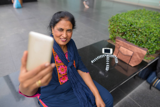 Mature Indian woman taking selfie with mobile phone in city - Фото, зображення
