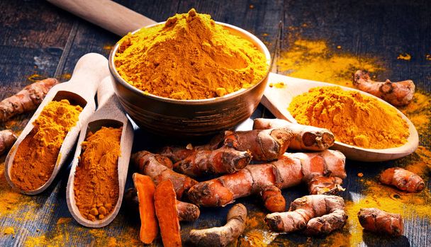 Composition with bowl of turmeric powder on wooden table. - Photo, Image