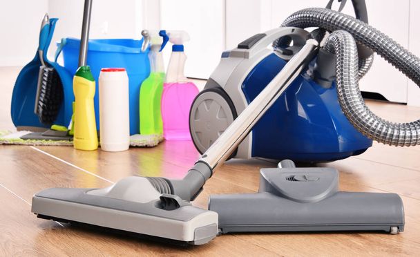Vacuum cleaner and variety of detergent bottles and chemical cleaning supplies on the floor - Photo, Image