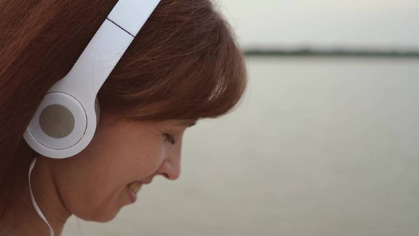girl in headphones walks along beach with tablet and listens to music, girl checks mail on a tablet online, close up - Photo, Image