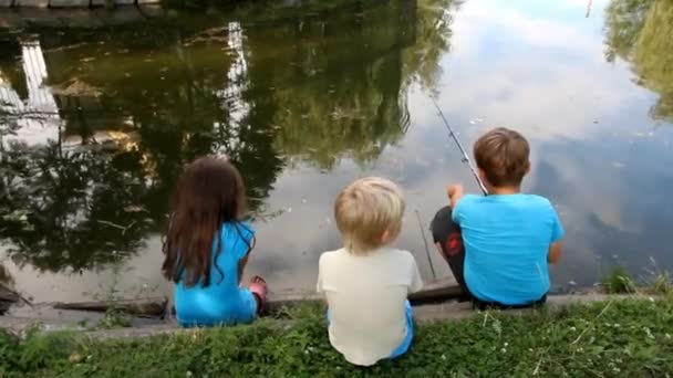 Három kis gyermek ül a tó partján, és horgászni - Felvétel, videó
