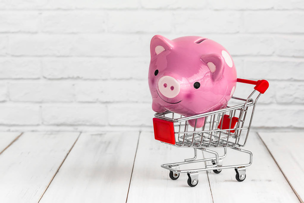 Piggy Bank in trolley shopping cart on white wood background with copy space. saving for shopping concept. - Photo, Image