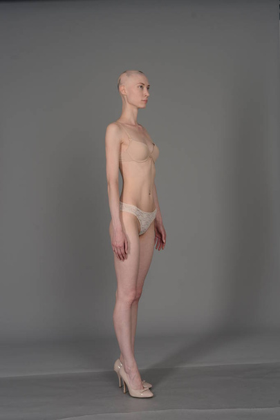 bald girl in beige lingerie posing on grey background - Photo, image