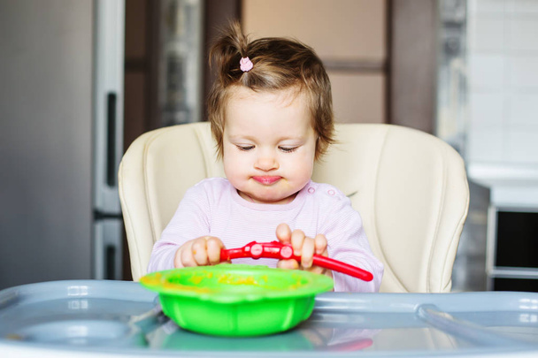 funny little baby eating vegetable puree sitting at table - Фото, изображение