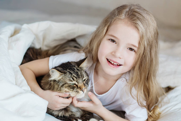 Charmante gelukkig klein meisje haar kat in bed liggen knuffelen  - Foto, afbeelding