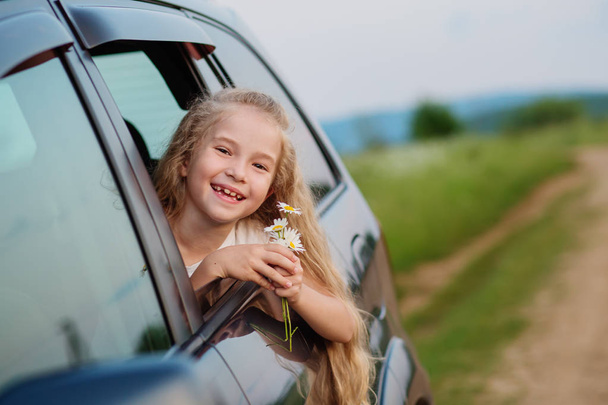 happy little girl in the car peeking out the window with a bouquet of chamomiles - Foto, Bild