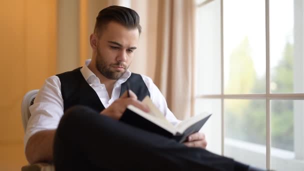 A man sitting on armchair and flips through a book - Séquence, vidéo