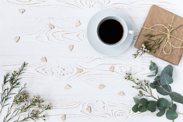 Top view of coffee, gift wrapped in kraft paper , hearts, flowers on white wooden table. Background with free space for text. Flat lay - Photo, Image
