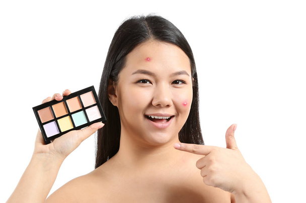 Retrato de mujer asiática joven con paleta de correctores para enmascarar el acné sobre fondo blanco
 - Foto, Imagen